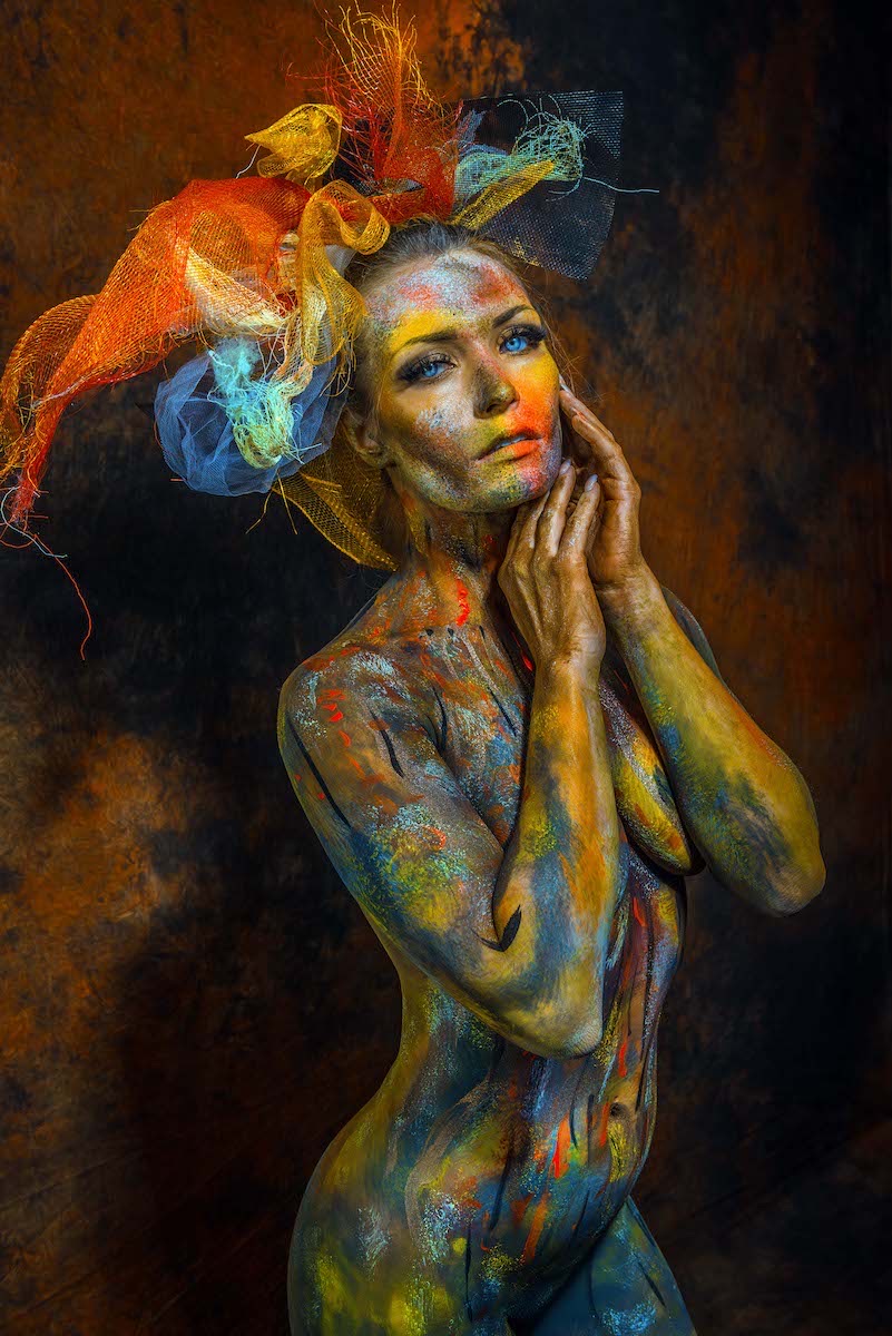 Scarlet meeting the camera in multicolor body paint and a fire-toned headpiece